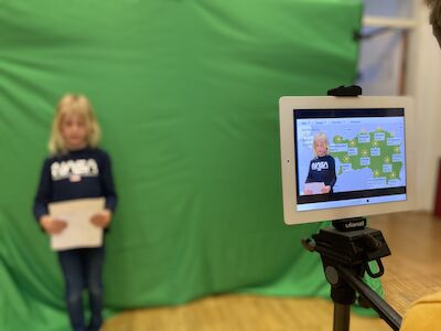 Kind steht vor einem Greenscreen, während es für einen Wetterbericht gefilmt wird.