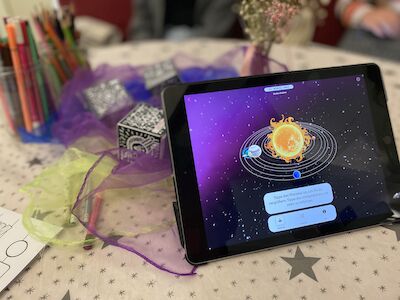 Tablet mit einer Sonnensystem-App auf einem Tisch mit Sternenmuster und Kunstbedarf.